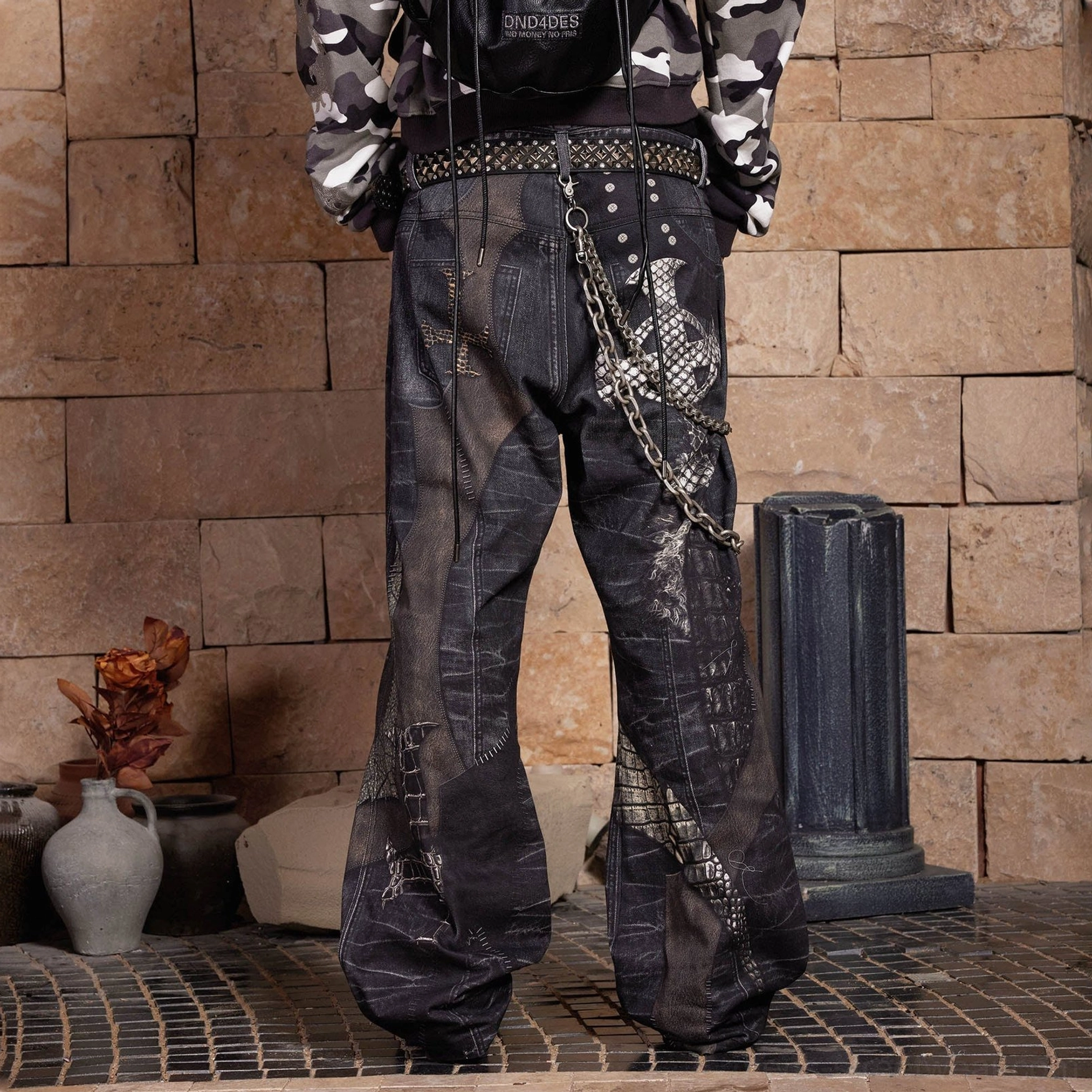 Back view of gothic dragon sword wide-leg jeans showing rear leg graphics, studded belt, layered metal chains, and loose dark denim silhouette