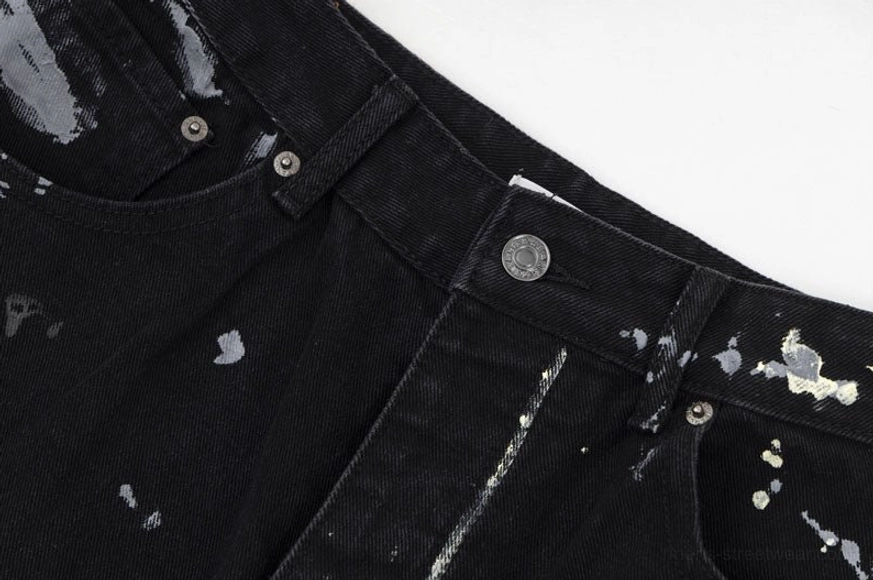 Metal denim button zipper fly and belt loops close-up on graffiti-print wide-leg jeans with small splatter artwork on waist fabric