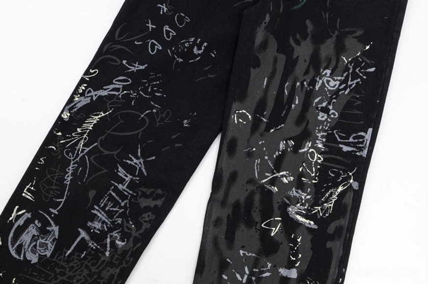 Dual pant leg side view close-up highlighting mixed handwritten graffiti tags and abstract ink splatters on streetwear wide-leg denim