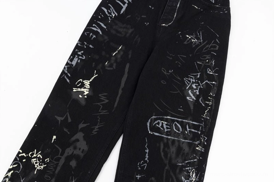 Close-up detail of lower pant legs showing stylized lettering graffiti tags and abstract splatter ink patterns on black denim fabric