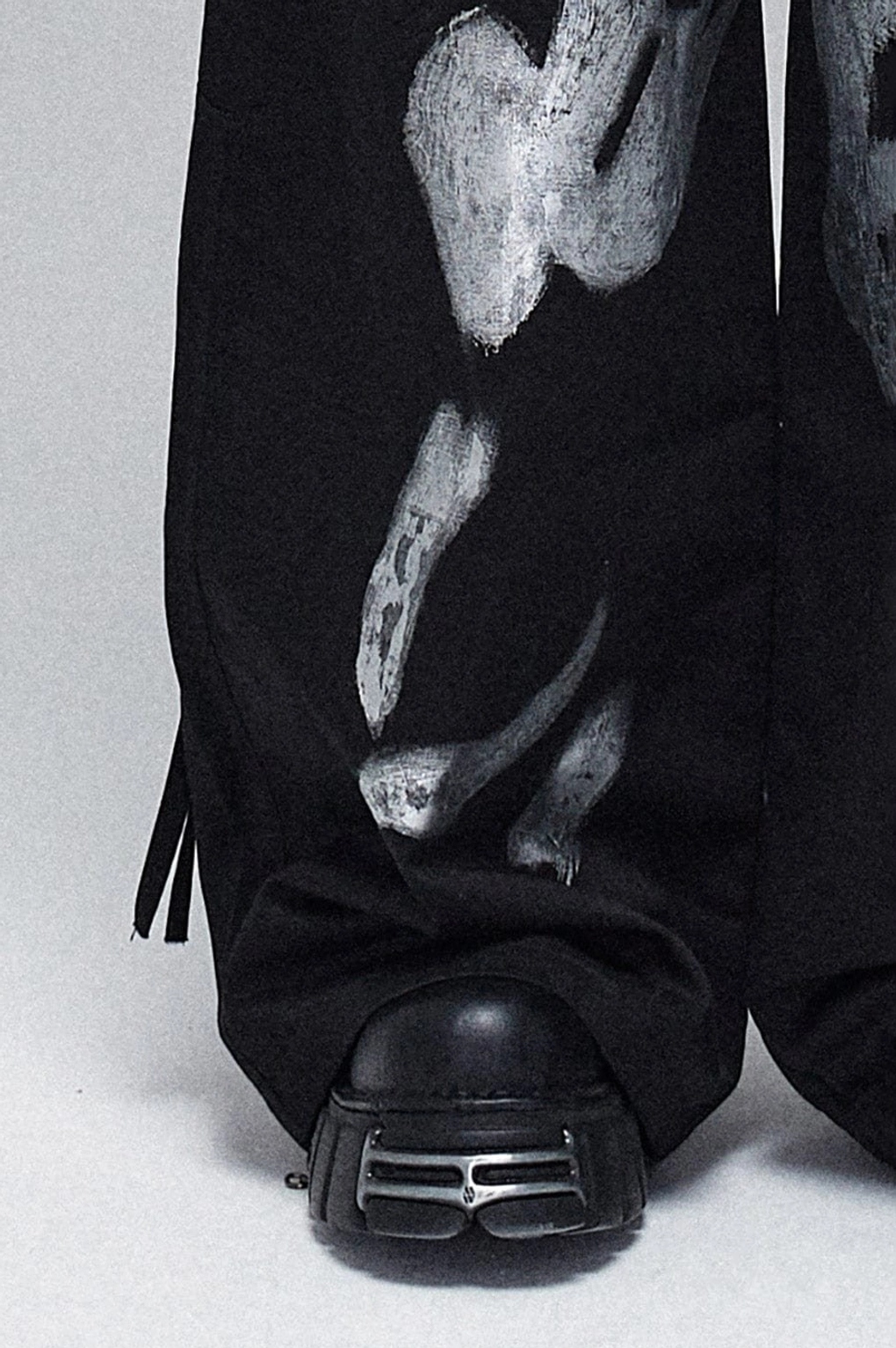 Lower-leg close-up of black silver graffiti cargo pants with adjustable hem drawstrings, heavy-duty fabric, and chunky platform boots