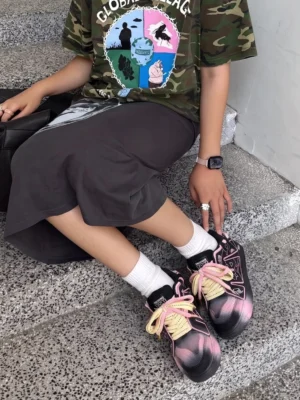 Model wearing black and pink graphic chunky streetwear sneakers with two-tone laces on concrete stairs