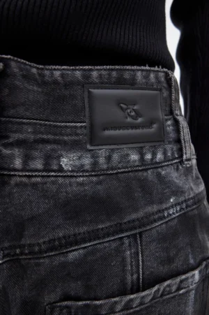 Close-up rear waist detail of graphite black distressed denim jeans showing leather patch belt loops washed texture and paint splatter finish