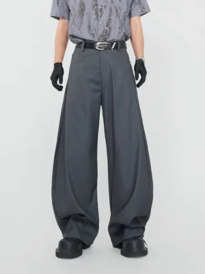 Front view of graphite grey ultra-wide pleated streetwear dress trousers styled with a printed shirt, leather belt, gloves, and chunky black shoes