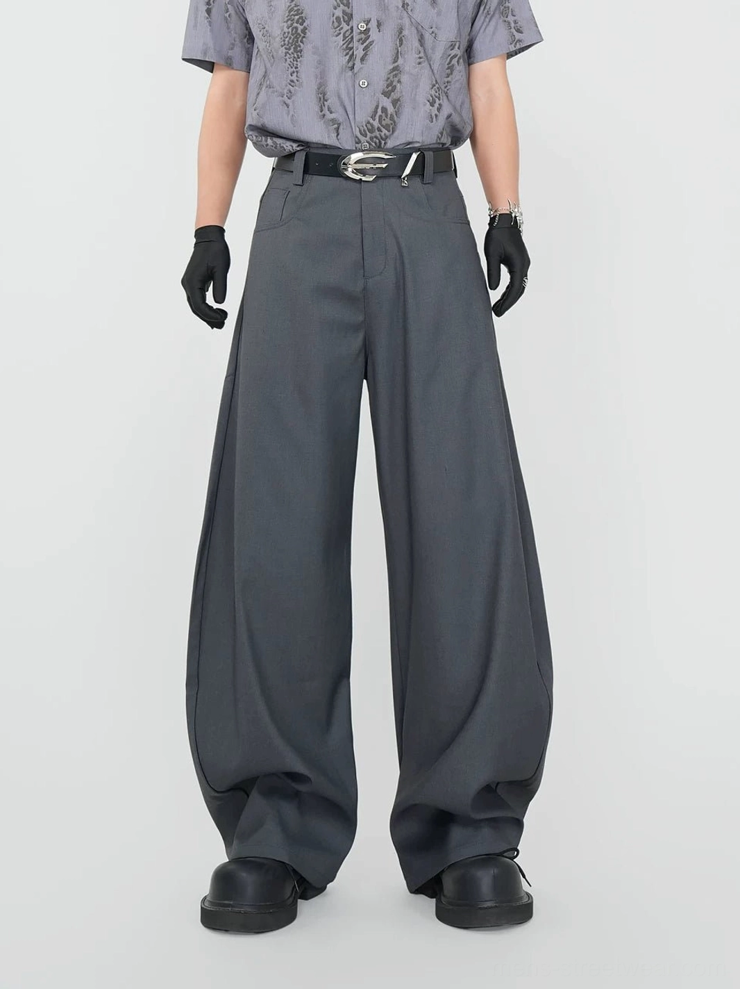 Front view of graphite grey ultra-wide pleated streetwear dress trousers styled with a printed shirt, leather belt, gloves, and chunky black shoes