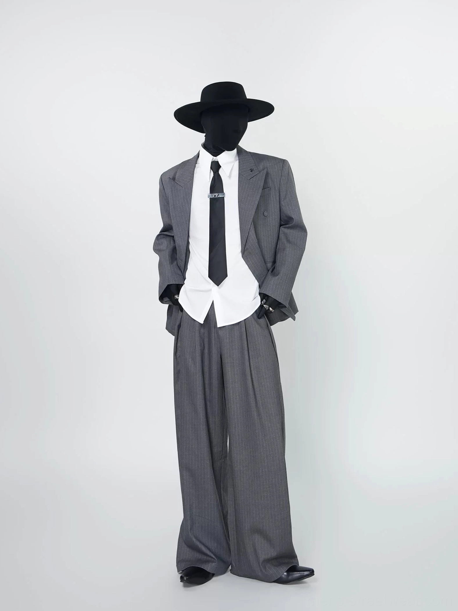 Grey pinstripe oversized double-breasted blazer styled open with white shirt black tie and wide-leg tailored trousers