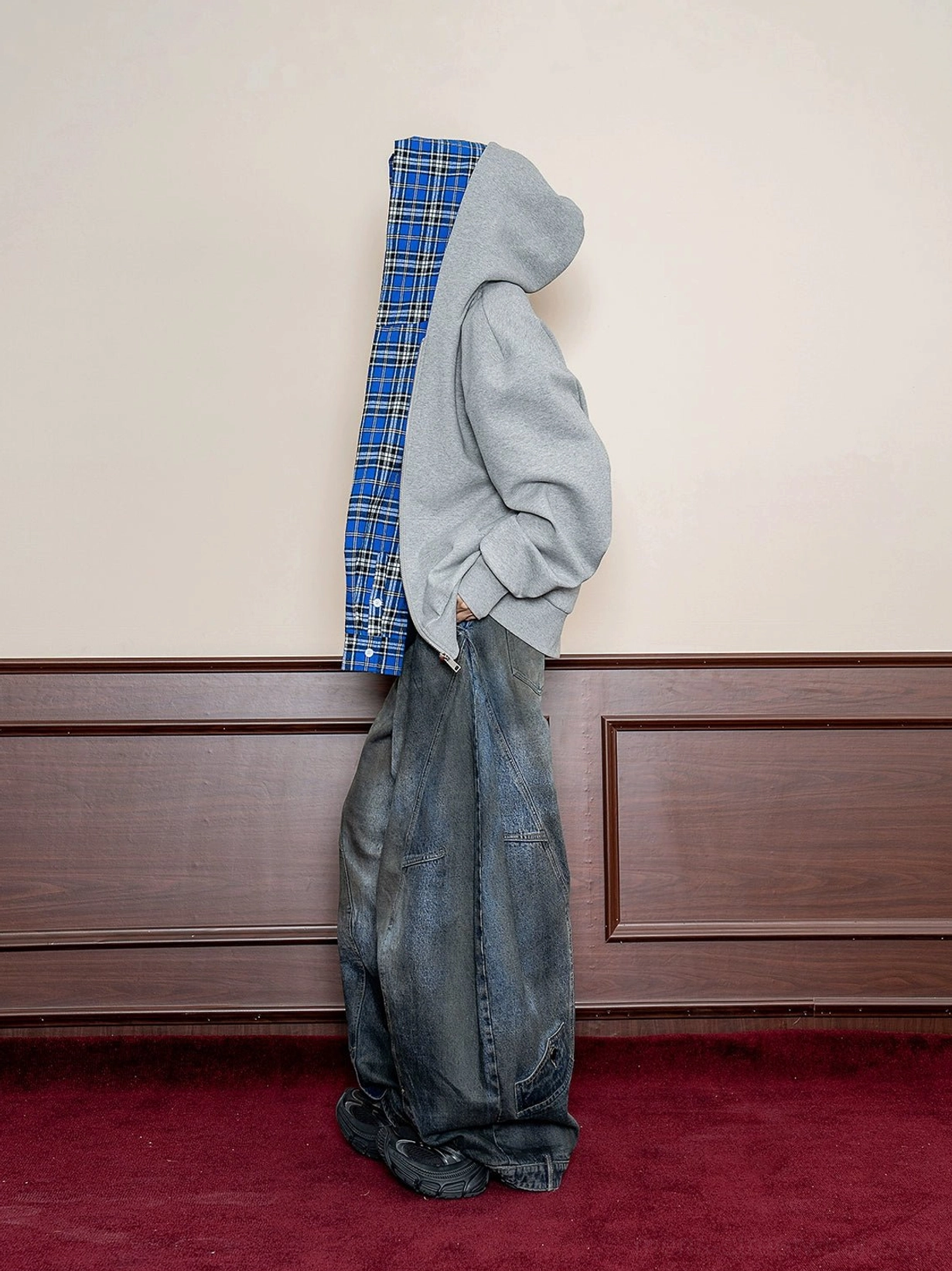 Rear side view of a gray oversized streetwear hoodie with exposed blue plaid hood lining paired with washed wide-leg denim