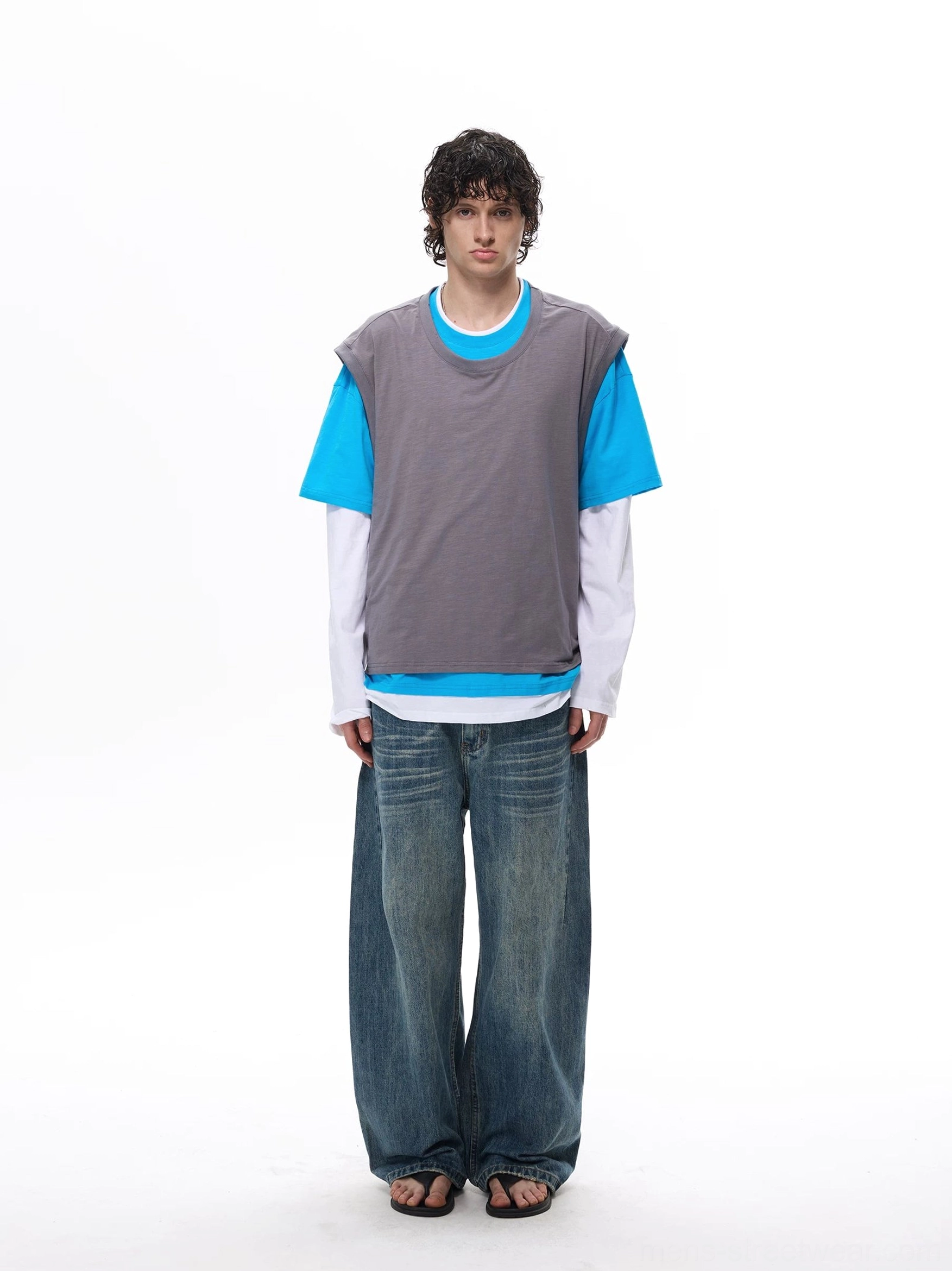 Front full-body view of a gray blue and white layered vest tee top worn with loose blue jeans and casual slides