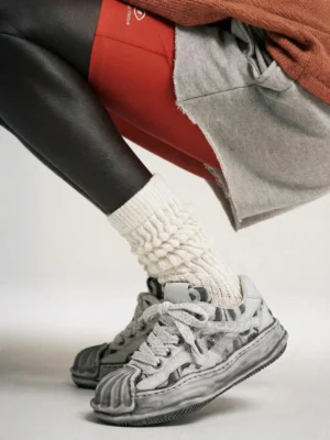 Gray camouflage shell toe skate sneakers worn with chunky knit socks cropped shorts and layered leggings in a casual streetwear outfit
