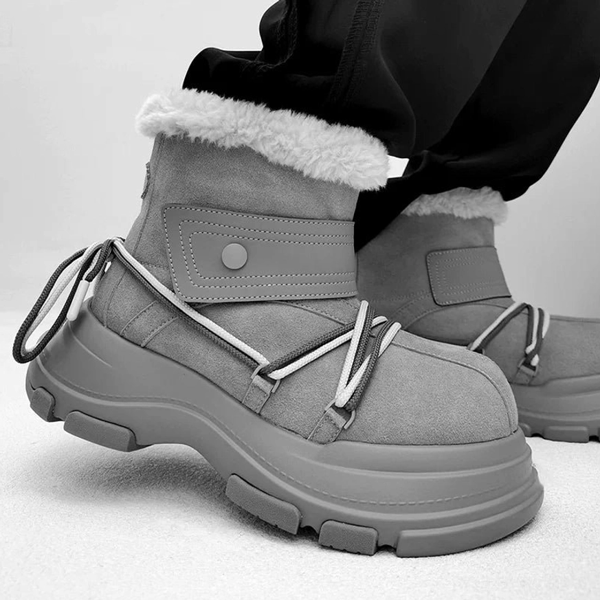 Gray chunky platform shearling snow boots with white wraparound laces, utility strap, and elevated rubber sole in a low-angle on-foot view