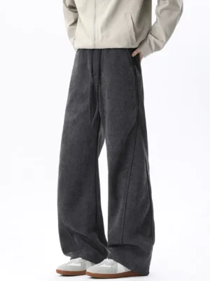 Gray fleece-lined herringbone wide-leg lounge trousers shown in a front three-quarter view with beige zip jacket and retro sneakers