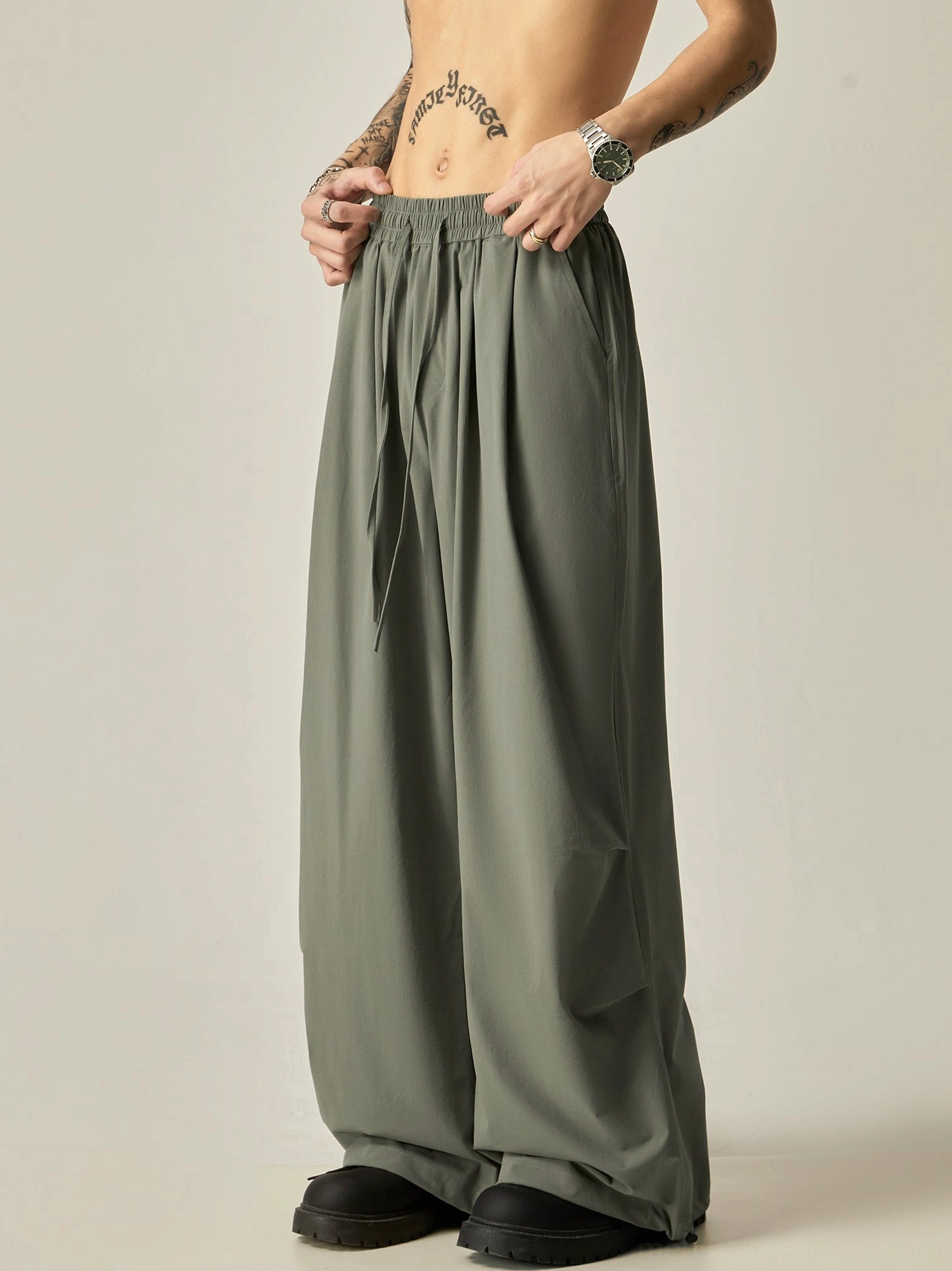 Gray green flowy wide leg drawstring pants for men shown from the front with a relaxed streetwear silhouette and elastic waistband
