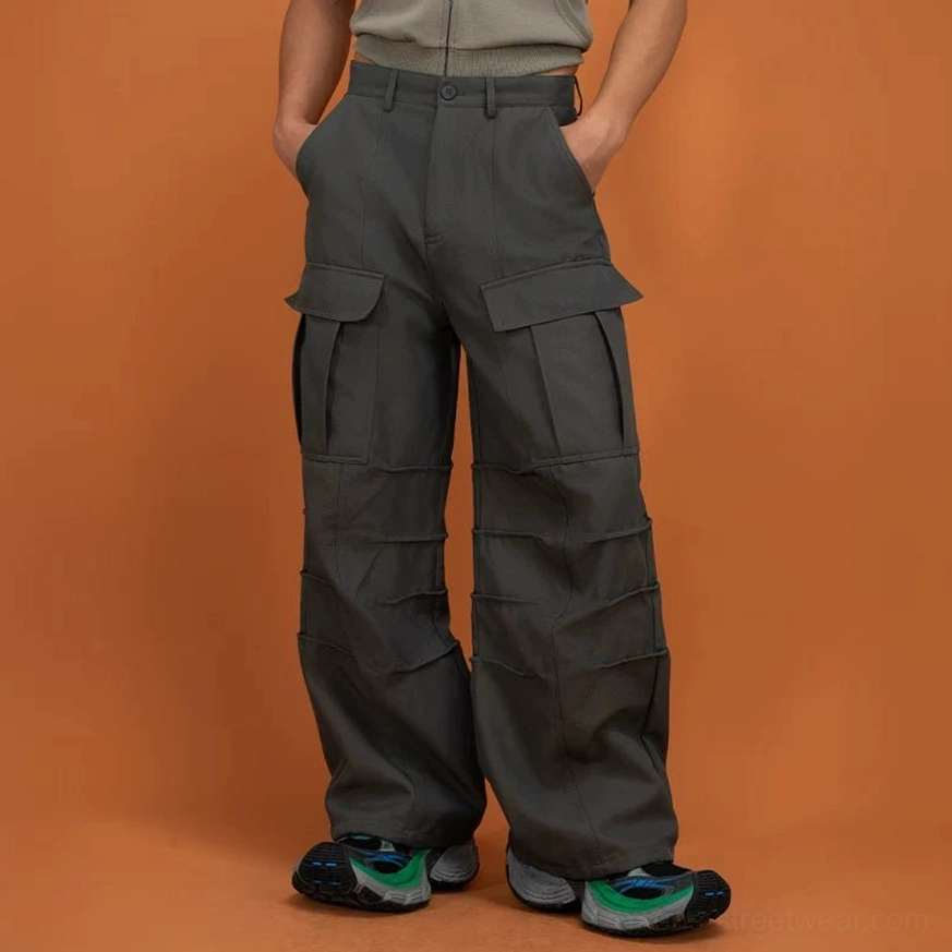 Dark gray green layered techwear cargo pants shown from the front three-quarter view with wide legs and utility pockets