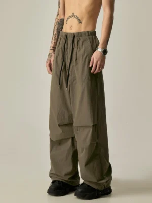 Side view of gray green relaxed drawstring cargo track pants with wide legs, utility side pockets, and adjustable cuffs