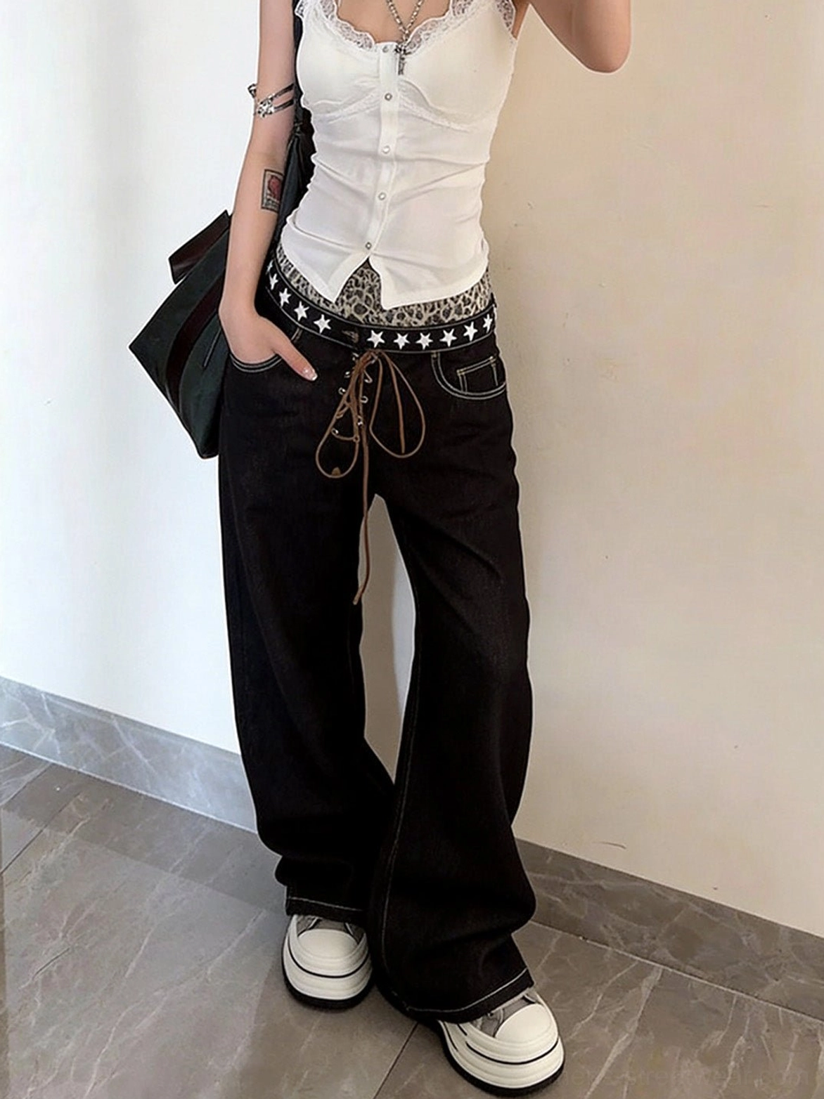 Female model wearing gray height-boosting platform sneakers with a white camisole and star-pattern high-waist black wide-leg jeans