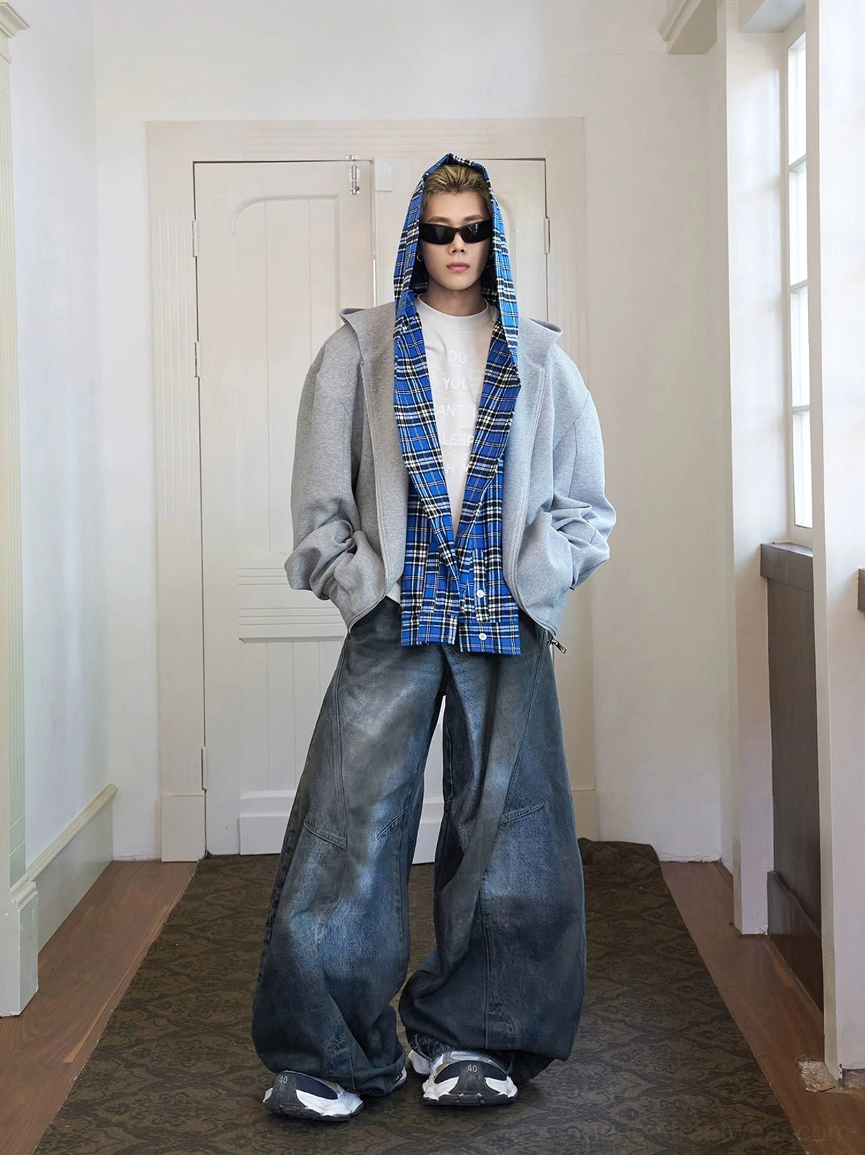 Front view of a relaxed gray oversized hoodie with contrasting blue plaid hood lining styled with a white tee and baggy dark denim