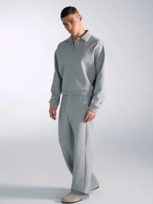 Male model wearing a heather gray oversized polo sweatshirt with relaxed drop shoulders in a minimalist streetwear studio