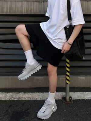 Gray leather platform casual sneakers styled with white T-shirt, black shorts, crew socks, and shoulder bag in an urban streetwear setting