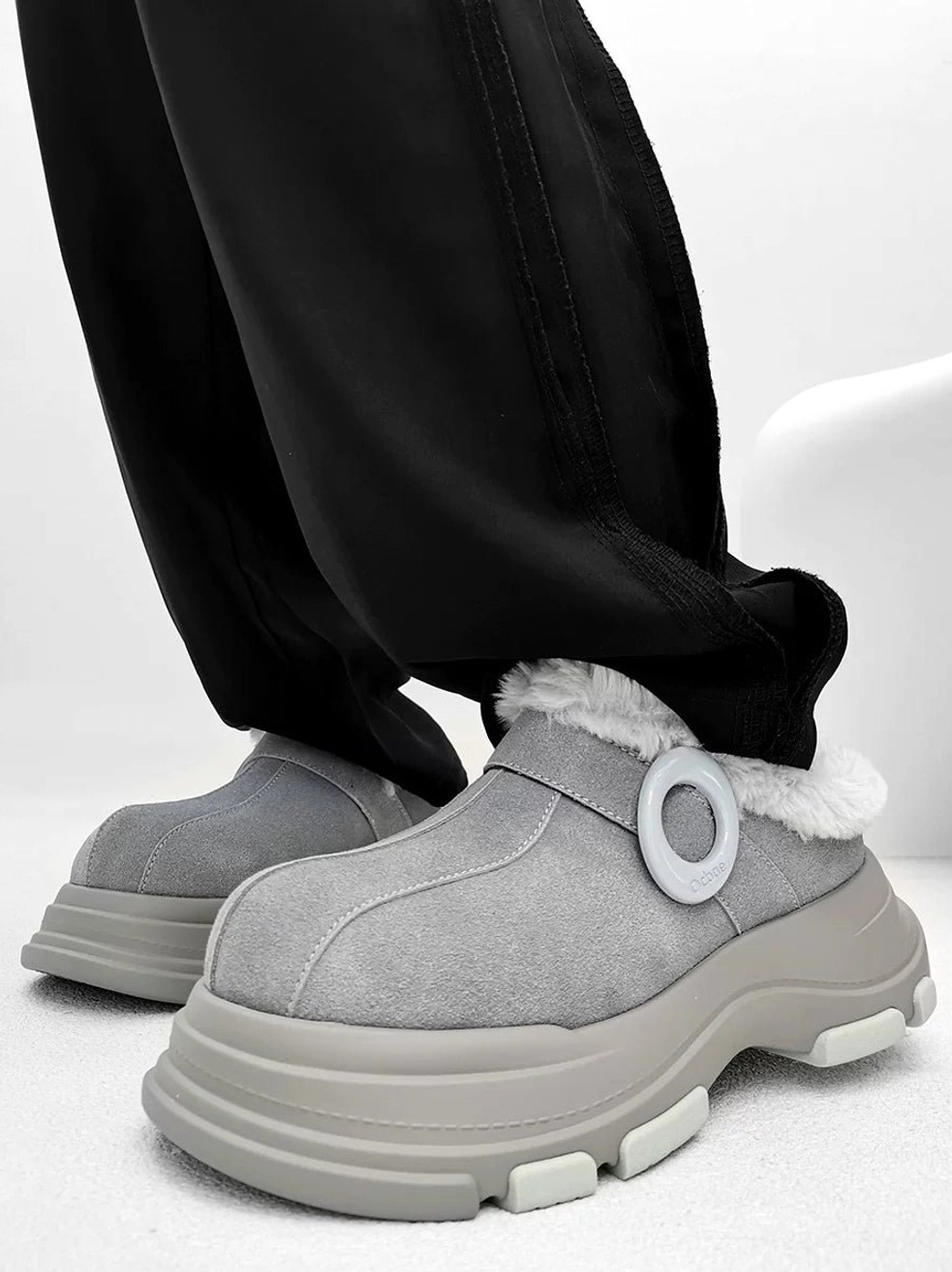 Gray platform fleece clog worn with black casual pants, featuring circular decorative ring, fluffy collar, and multi-section chunky outsole