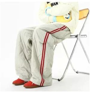 Gray padded quilted streetwear pants with red stripes styled with a cream sweatshirt and red sneakers in a seated pose