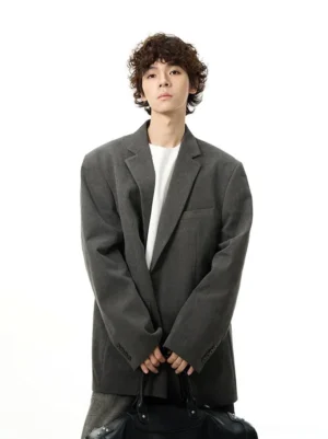 Gray relaxed fit tailored streetwear blazer on male model in three quarter front view with black leather duffle bag