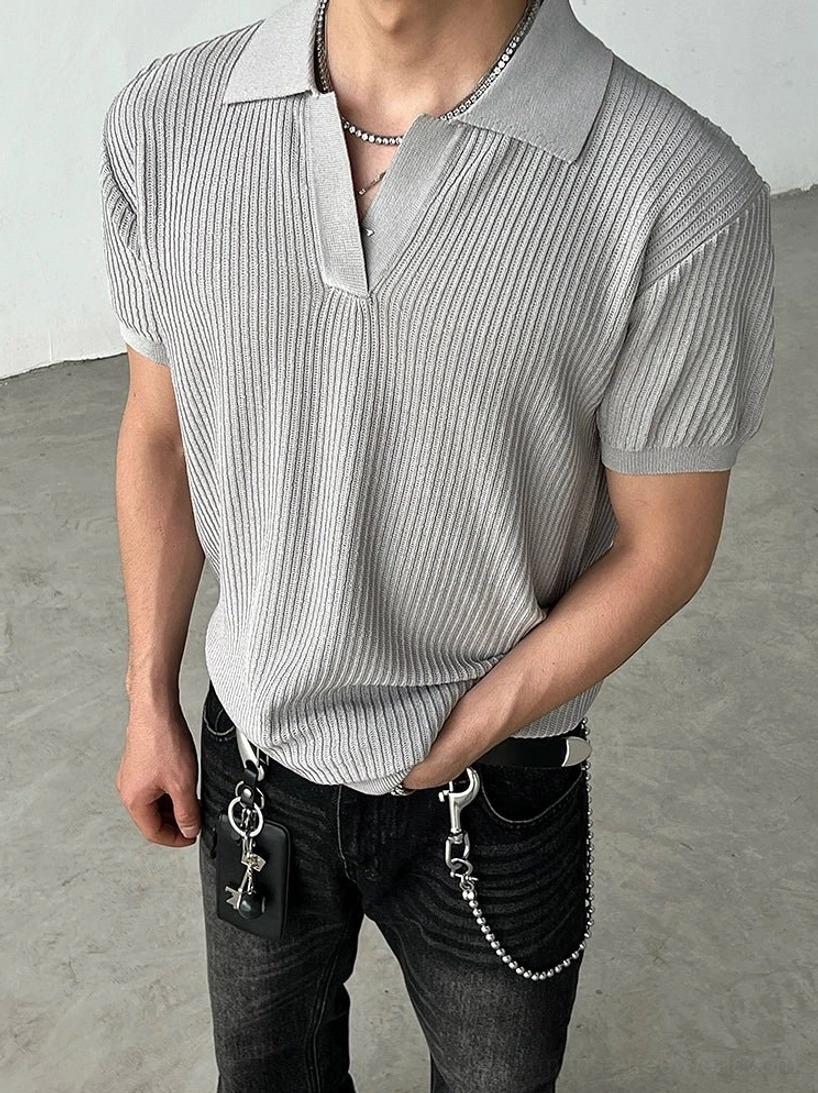 Full-body view of a model wearing a gray ribbed knit short-sleeve polo shirt with black washed jeans and chain details