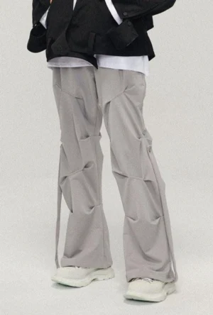 Gray sculpted wide-leg streetwear pants with gathered pleats and adjustable side drawstrings paired with chunky white sneakers