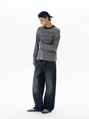 Three quarter side view of a relaxed gray striped long sleeve slogan tee with cropped regular hem, baggy jeans, and slide sandals
