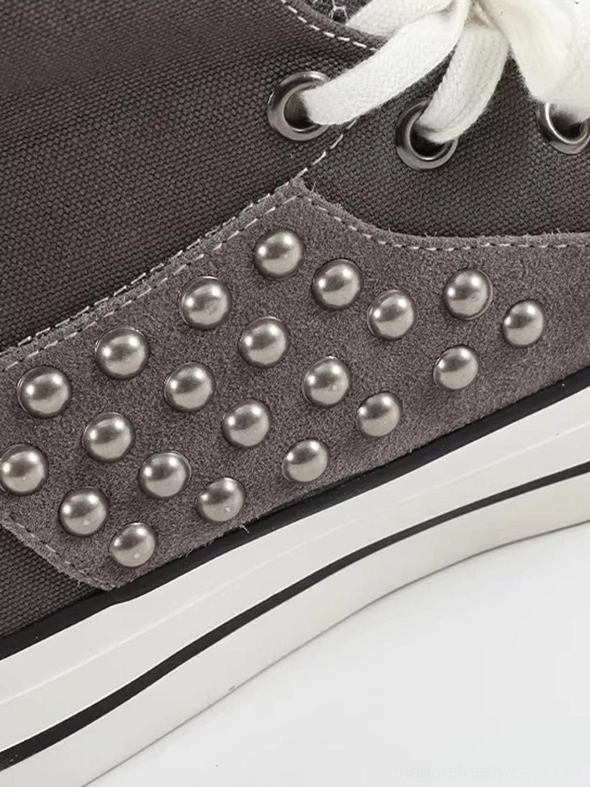 Close-up of silver round metal studs on the gray suede-textured side panel with metal eyelets, white midsole, and black stripe