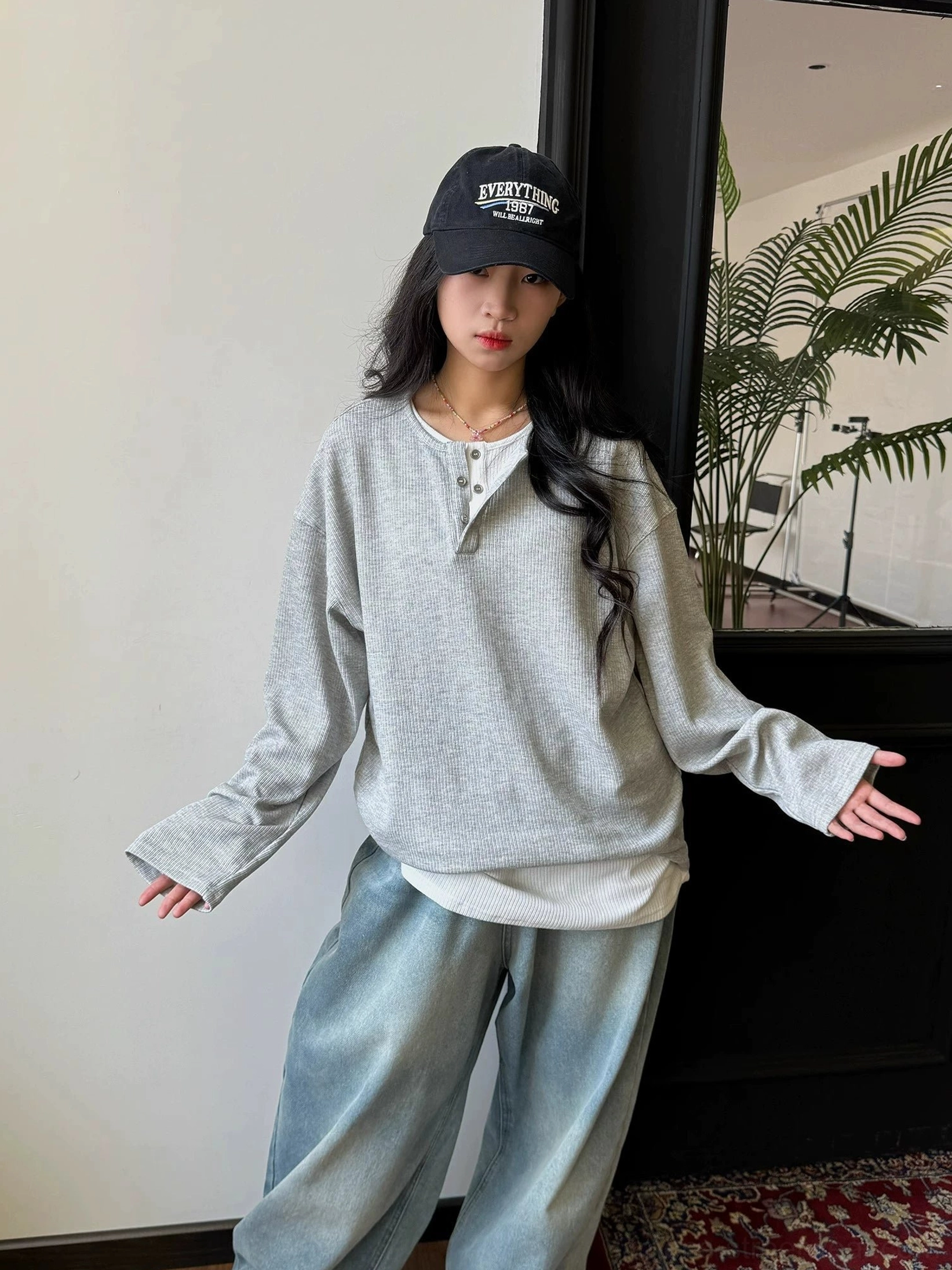 Female model wearing an open relaxed heather gray waffle knit Henley shirt with washed wide-leg jeans and layered hem styling
