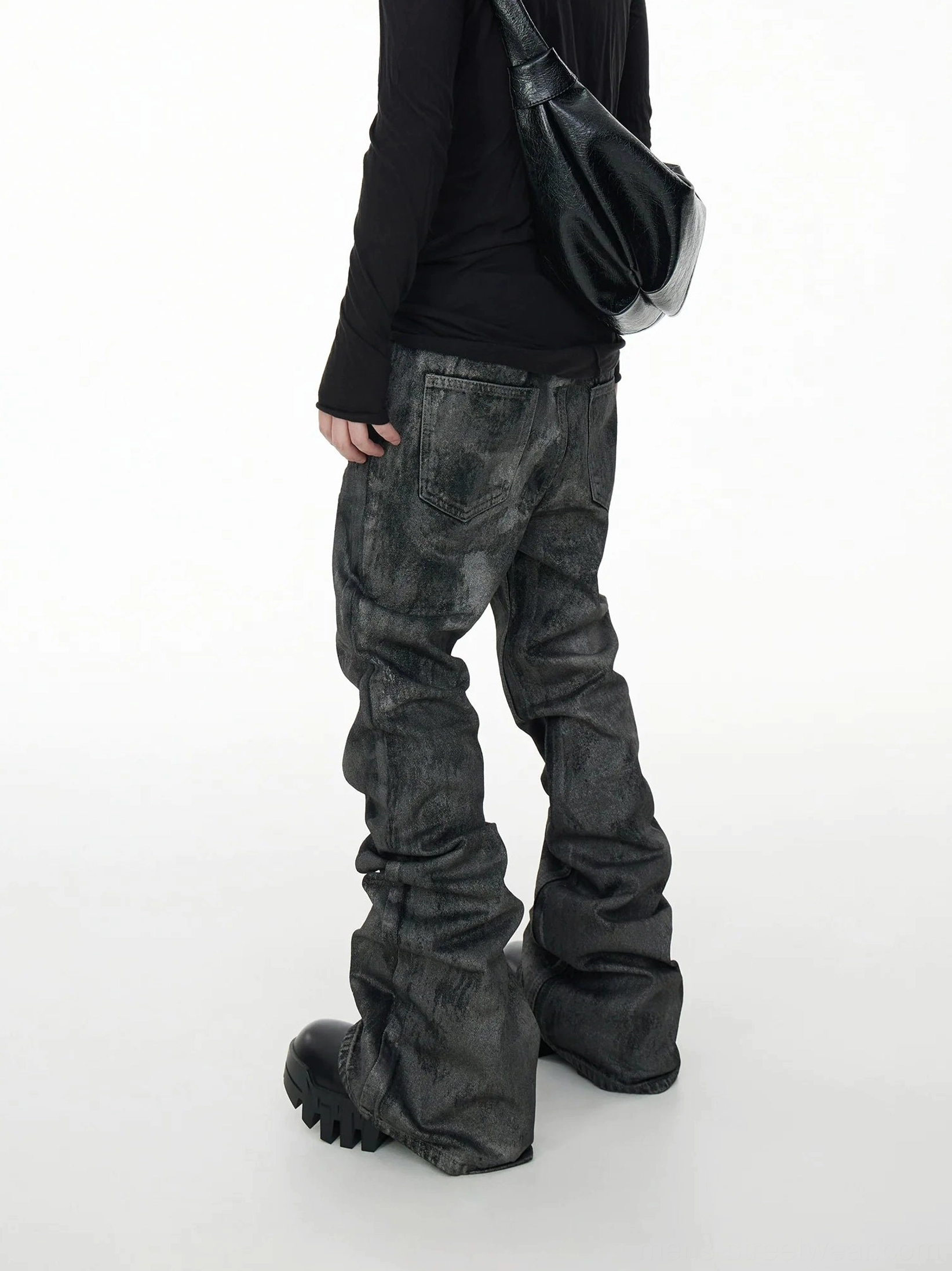 Rear three-quarter view of gray washed stacked jeans with oversized back pockets, voluminous legs, black platform boots, and leather shoulder bag