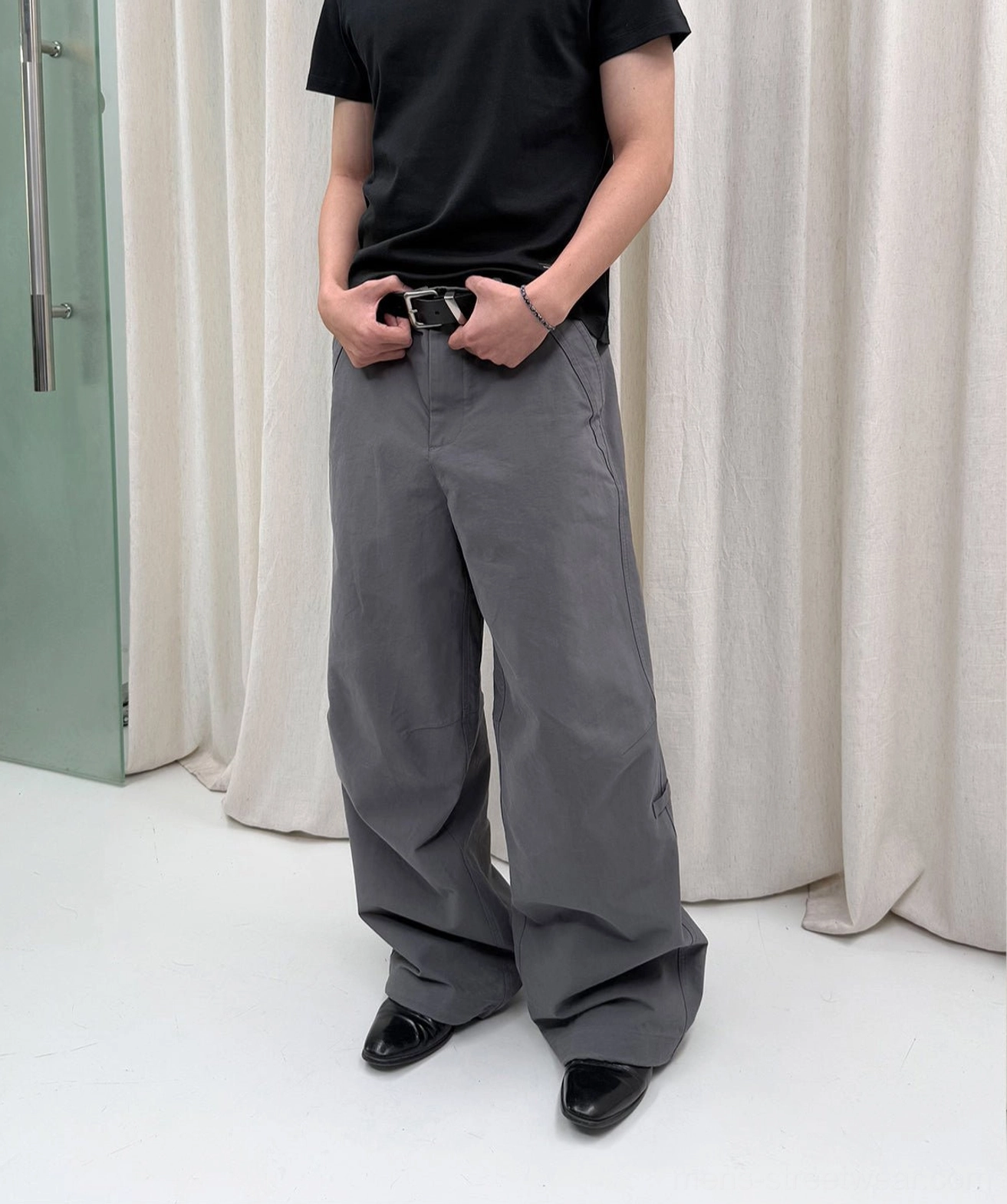 Gray washed wide-leg trousers shown in a full front view with a relaxed silhouette, black leather belt, and formal-inspired shoes