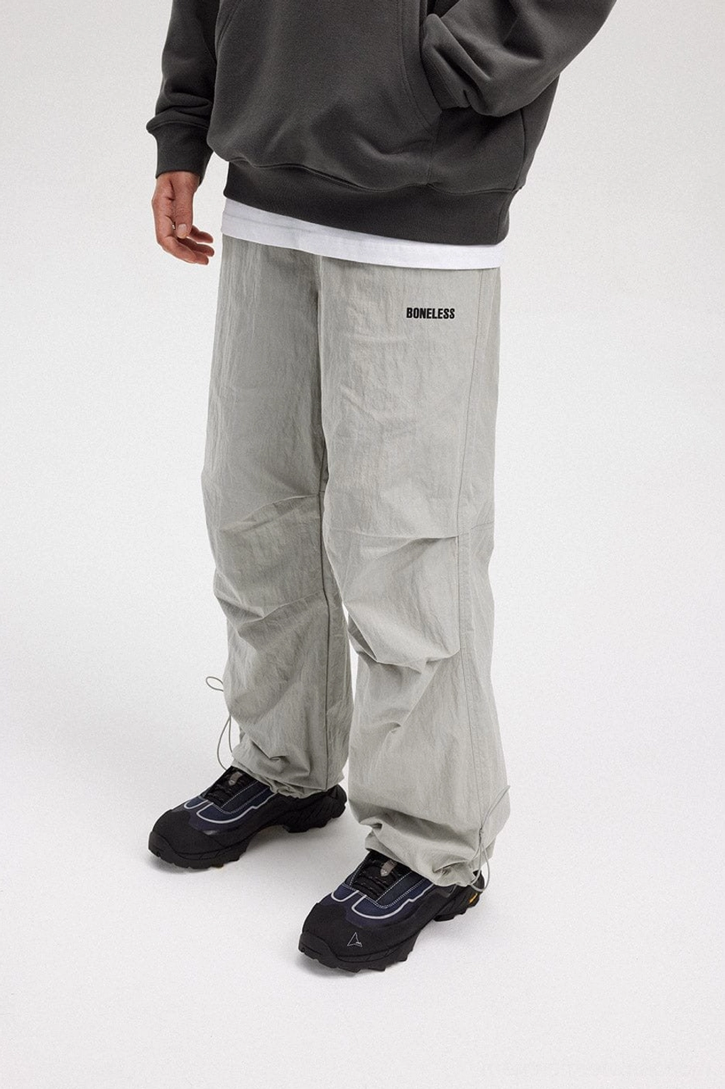 Side view of gray crinkled wide-leg track pants showing the relaxed utility-inspired silhouette and adjustable hem