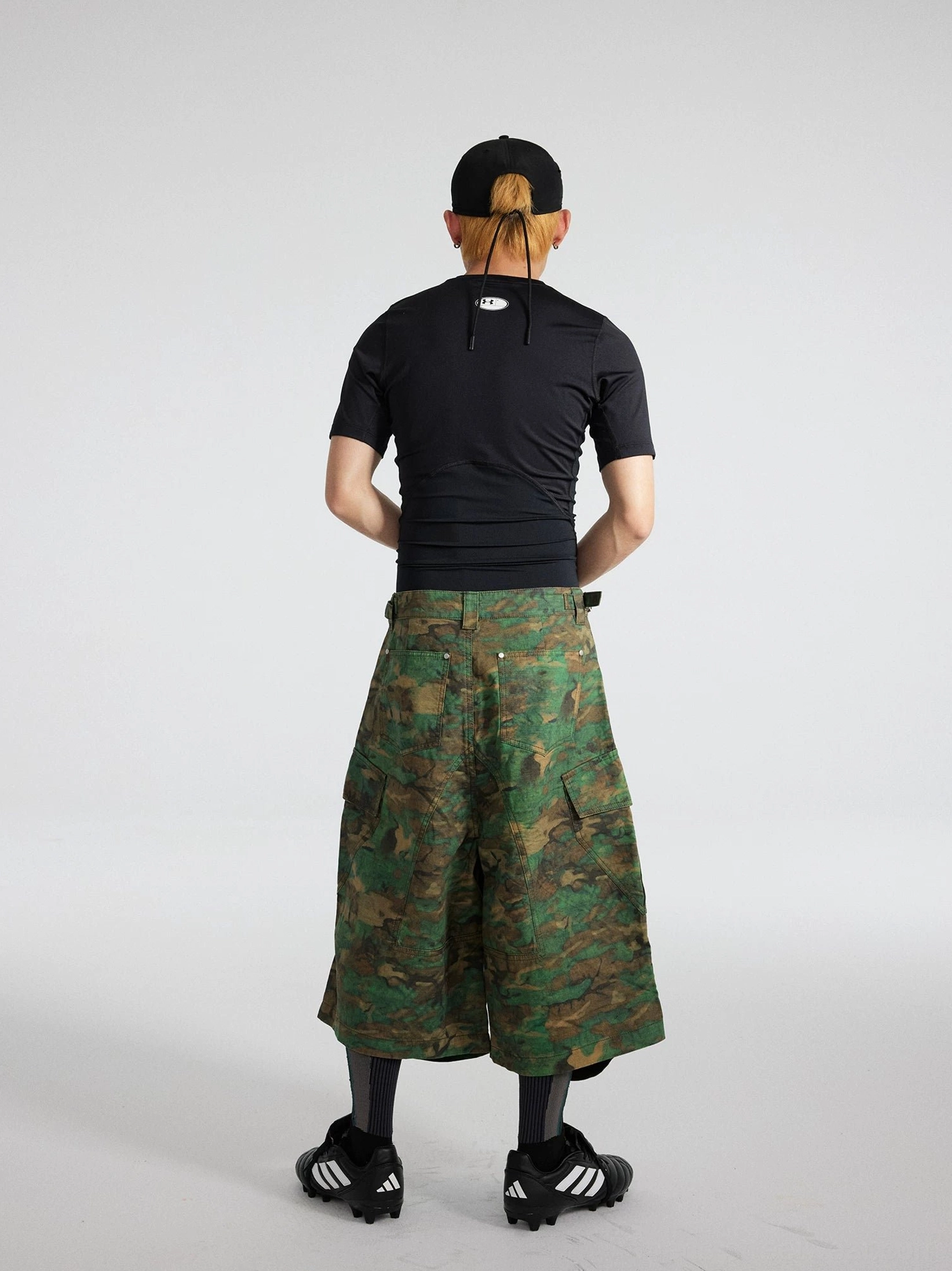 Rear view of green camouflage 3/4 cargo shorts showing the back waistband structure, relaxed wide-leg fit, and utility pocket details