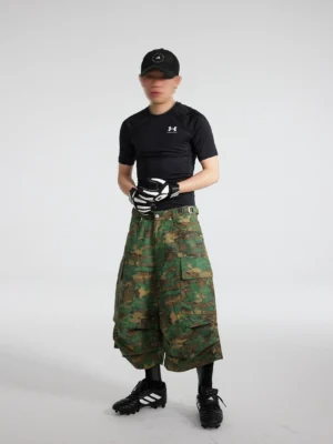 Full-body front view of a male model wearing oversized green camo cargo shorts with large utility pockets and a Korean streetwear outfit