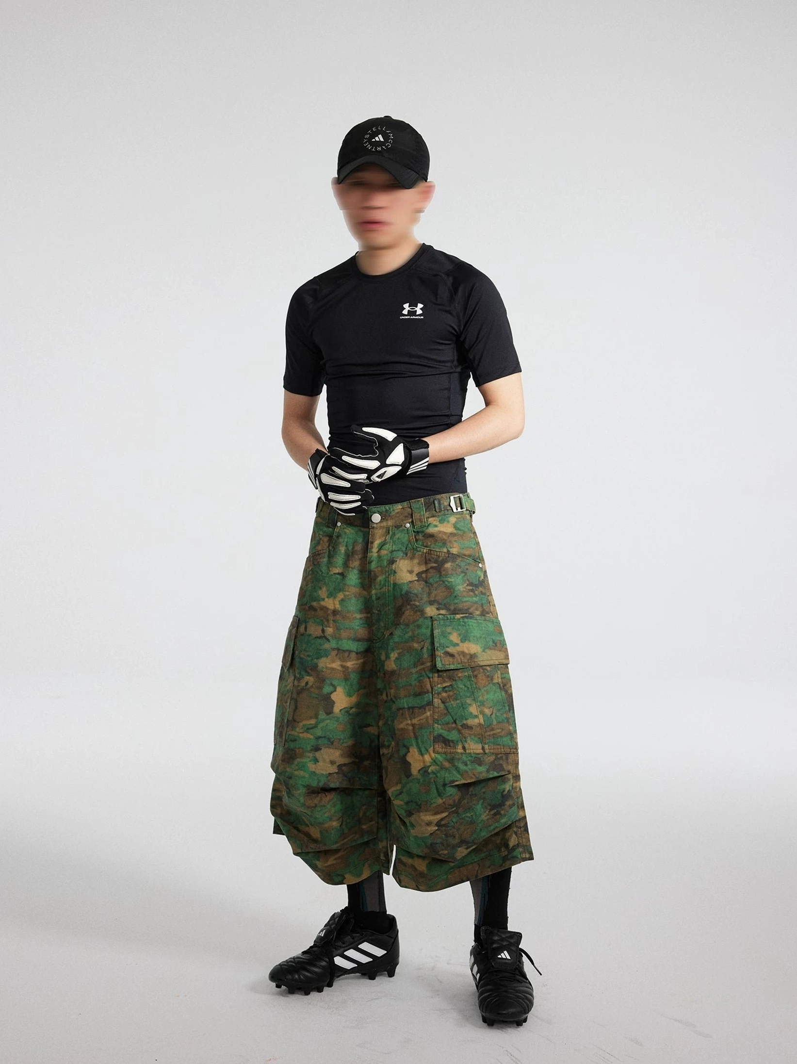 Full-body front view of a male model wearing oversized green camo cargo shorts with large utility pockets and a Korean streetwear outfit
