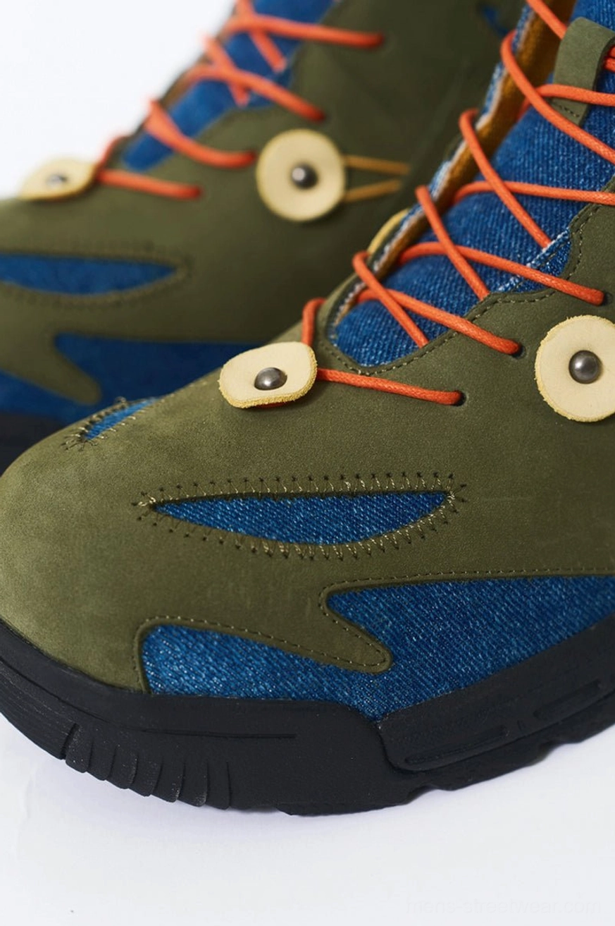 Close-up of green denim and suede hiking boot toe with orange laces, circular decorative buckles, and textured matte suede paneling
