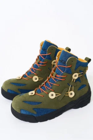 Green denim and suede outdoor hiking boots with orange round laces, circular buckle details, and thick black rugged anti-slip outsole shown from a front three-quarter view