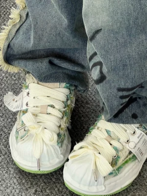 Pair of green frayed textile platform sneakers worn with distressed denim jeans, showing oversized bow laces and raised sculpted soles from above