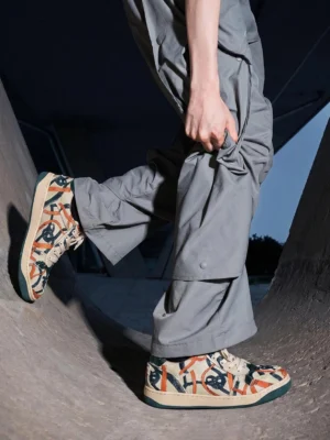 Green graffiti canvas low-top sneakers worn with gray cargo pants at an outdoor skatepark ramp, showcasing a casual skate-inspired streetwear outfit