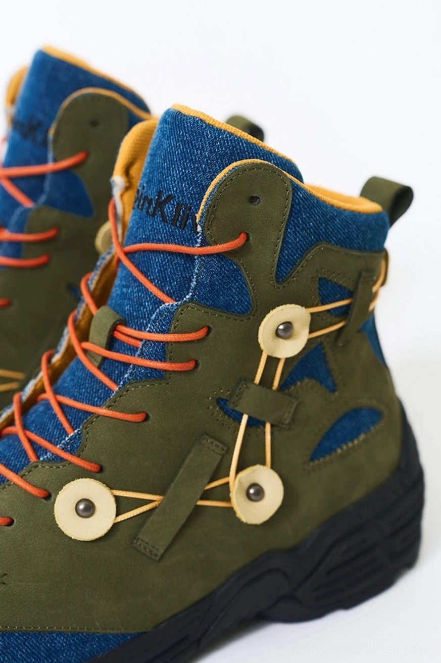 High-top green suede hiking boots with denim ankle collars, yellow inner lining, orange laces, and circular lace buckles shown in a side close-up