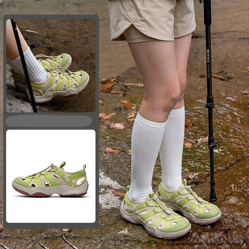 Green and yellow hybrid water hiking sandals worn with white socks on a wet rocky hiking trail, featuring closed toe and rugged traction outsole