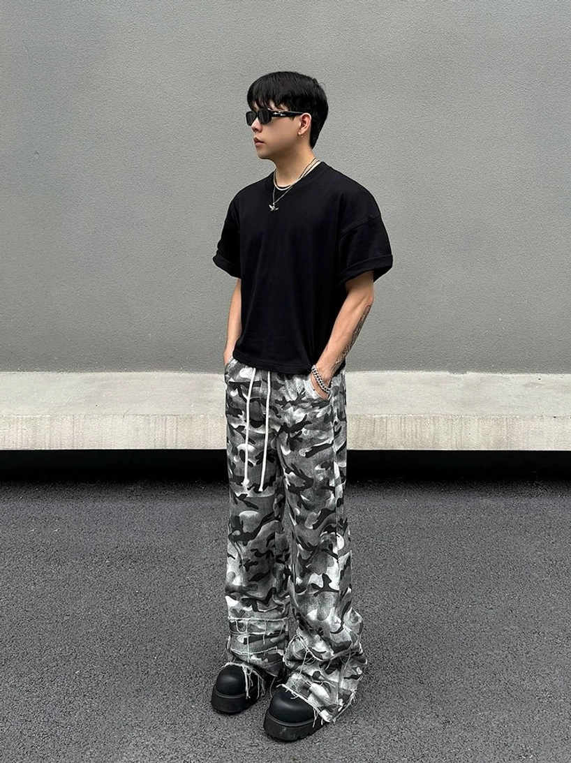 Styled side front view of grey abstract camouflage cargo pants with a loose silhouette, black T-shirt, sunglasses, silver jewelry, and platform footwear