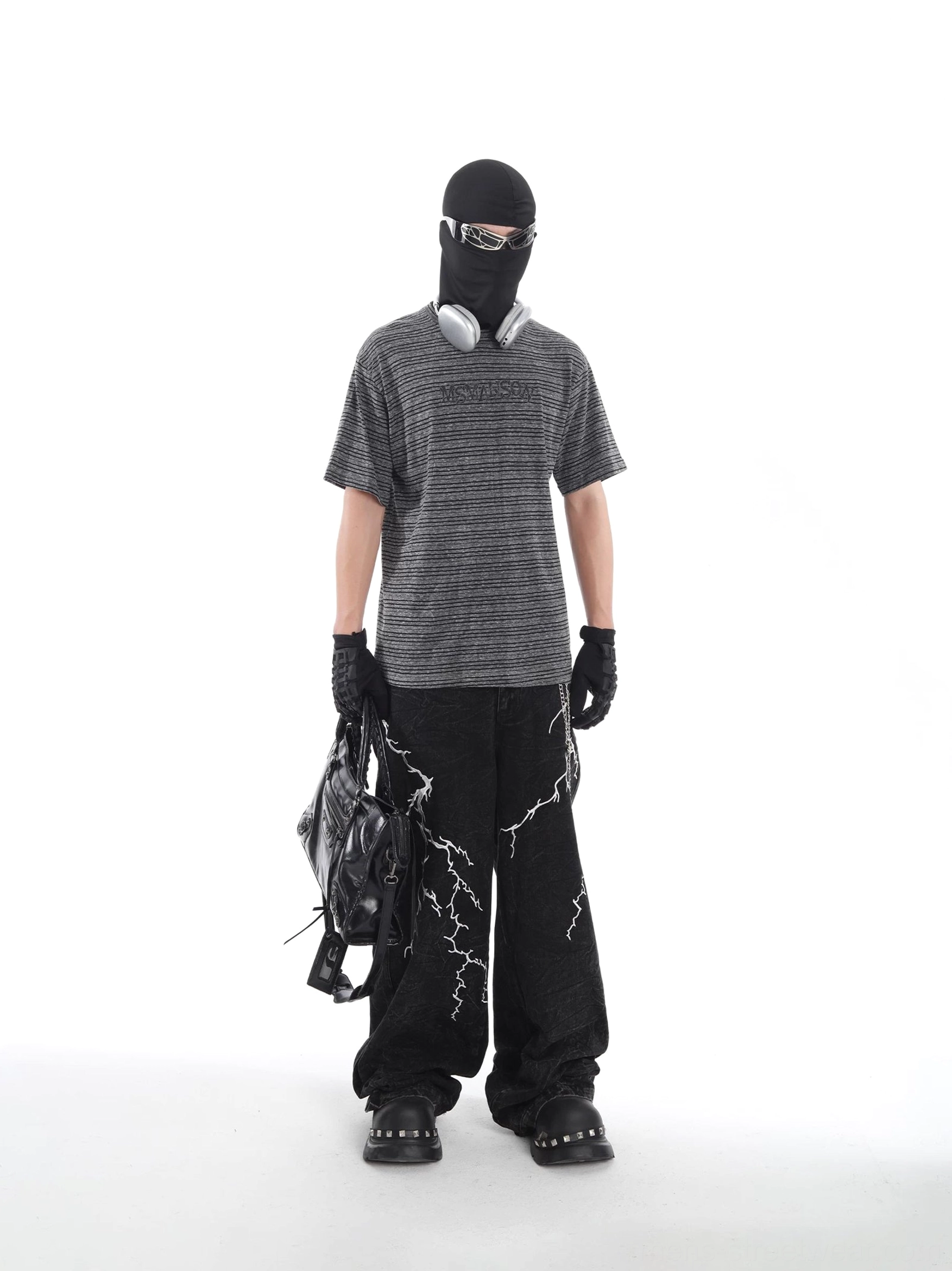 Full outfit view featuring a grey black striped oversized streetwear T-shirt styled with wide-leg black trousers, motorcycle bag, and platform shoes