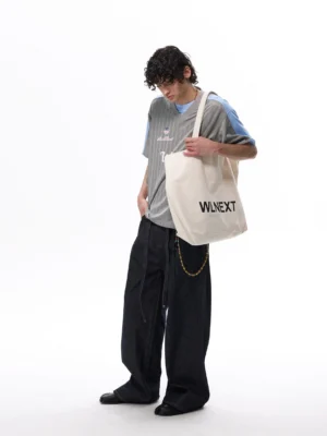 Full-body view of a model wearing a relaxed grey and pale blue soccer jersey T-shirt with dark wide-leg denim and a waist chain in contemporary streetwear style