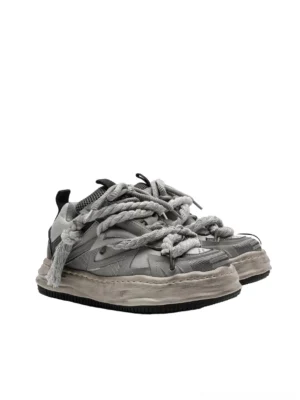 Grey distressed rope-lace chunky sneaker shown from the side with oversized twisted laces, mesh panels, geometric upper construction, and a faded thick sole