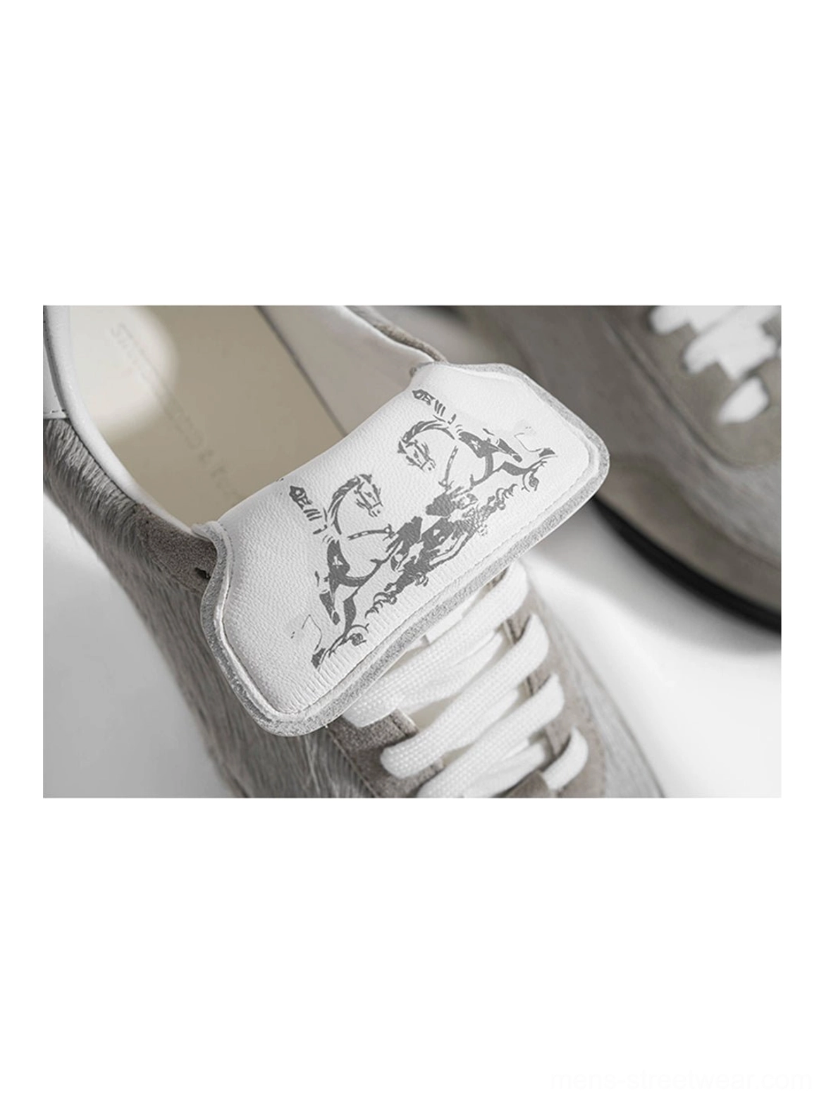 Front close-up of grey fur-lined platform sneakers with white leather tongue, artistic printed detail, flat white laces, and fuzzy upper