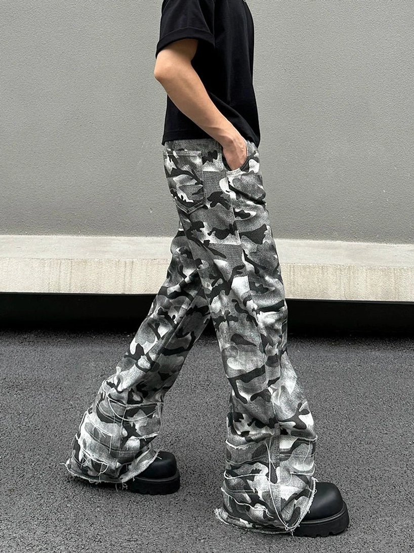 Side walking view of grey ghost camo cargo pants with a distorted wide-leg cut, relaxed pockets, stacked hems, and chunky black platform shoes