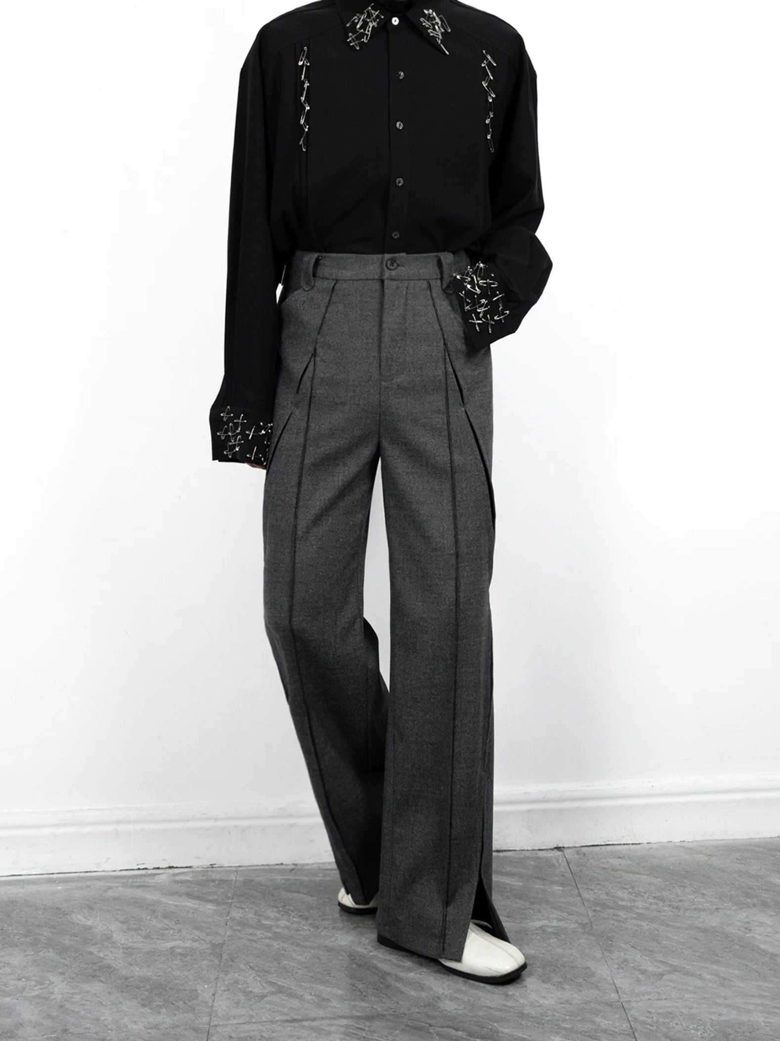 Side three-quarter view of high-waisted grey tailored trousers with front pleats, central crease, wide legs, and split hems