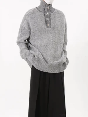 Front three-quarter view of a grey marled oversized button-neck knit sweater with dropped shoulders, ribbed stand collar, relaxed streetwear fit, and black wide-leg trousers